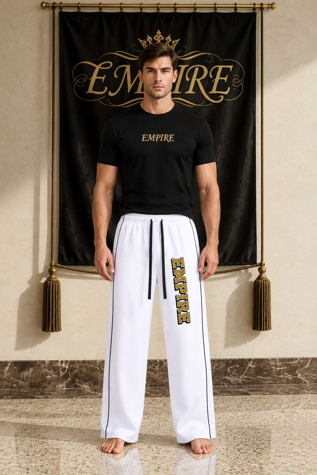 White men's EMPIRE straight-leg sweatpants with black piping and vertical gold wordmark, front view on barefoot male model