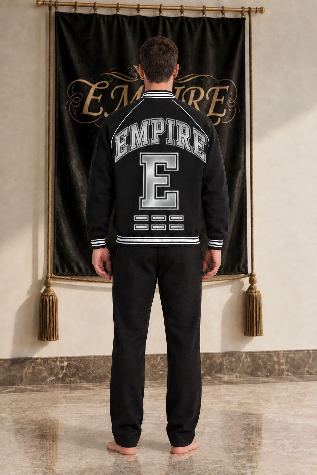 Black men's EMPIRE raglan varsity jacket with large silver collegiate wordmark and E back artwork, rear view on barefoot male model