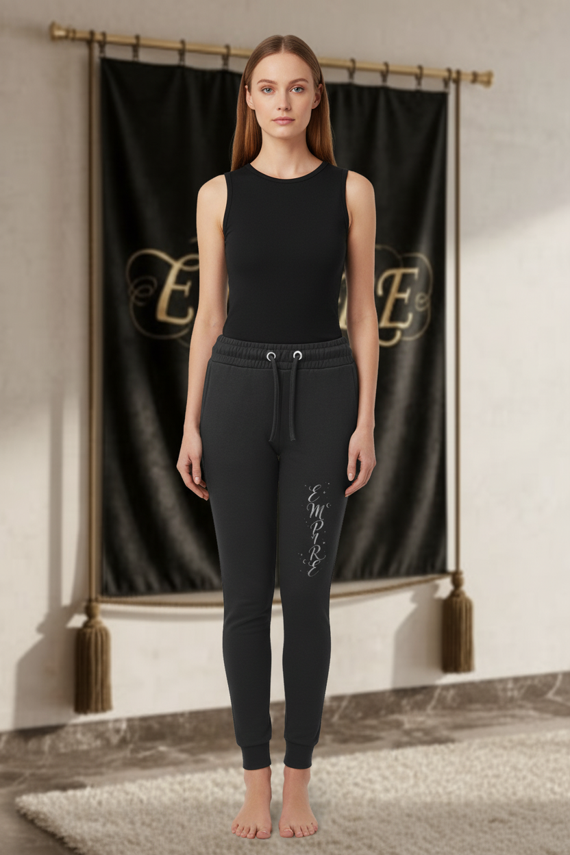 Femme portant le jogger EMPIRE noir ajusté avec cordons, œillets argentés, chevilles côtelées et script EMPIRE vertical clair, vue de face.