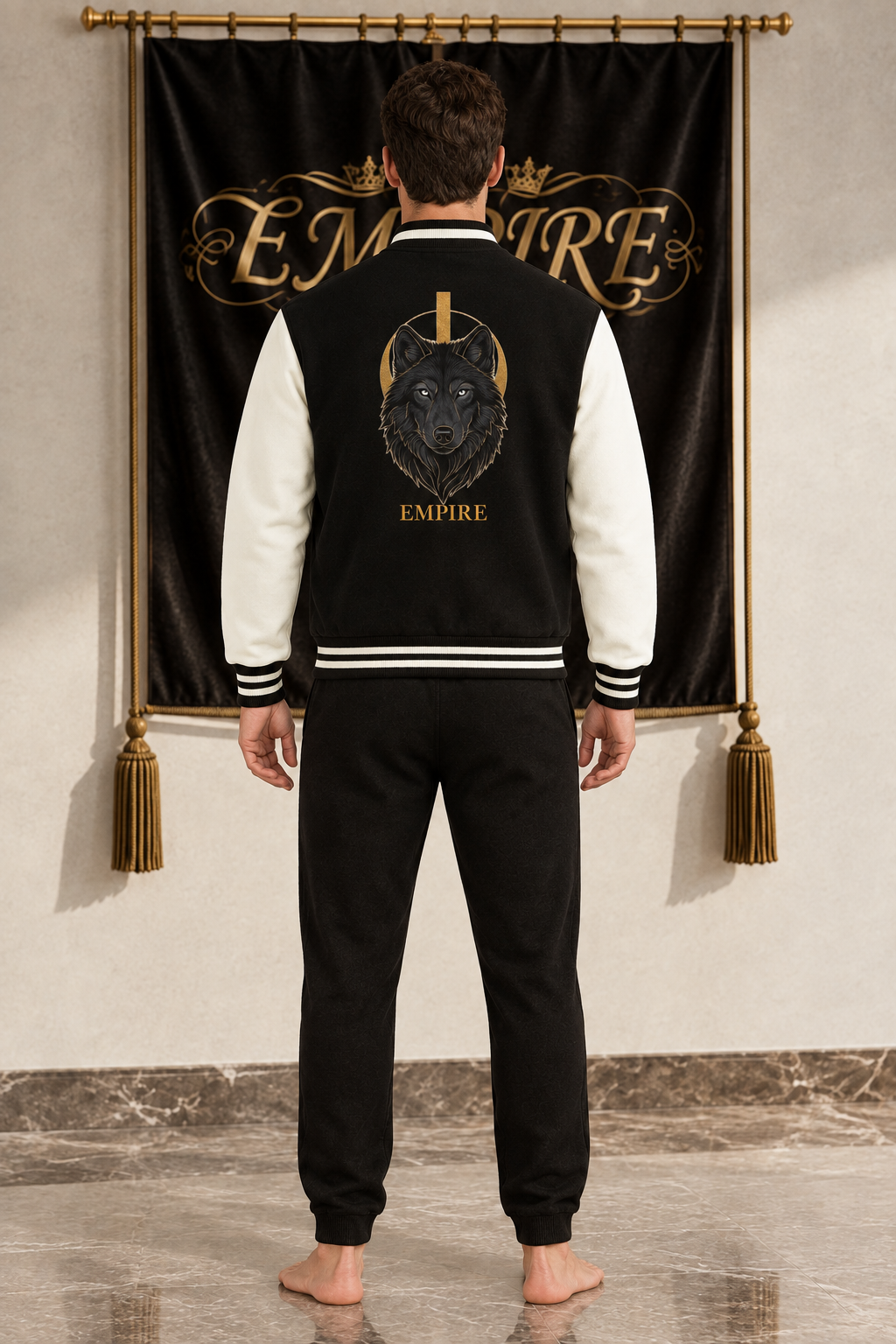 Black and ivory men's EMPIRE fleece varsity jacket with black wolf and gold eclipse back graphic, rear view on barefoot male model