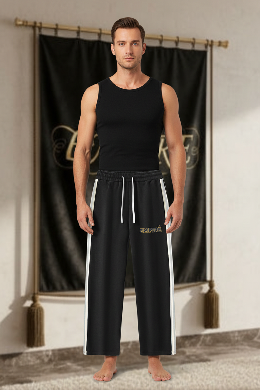 Homme portant un pantalon EMPIRE noir à bandes latérales blanches, cordons blancs et logo EMPIRE bleu et or, vue de face.