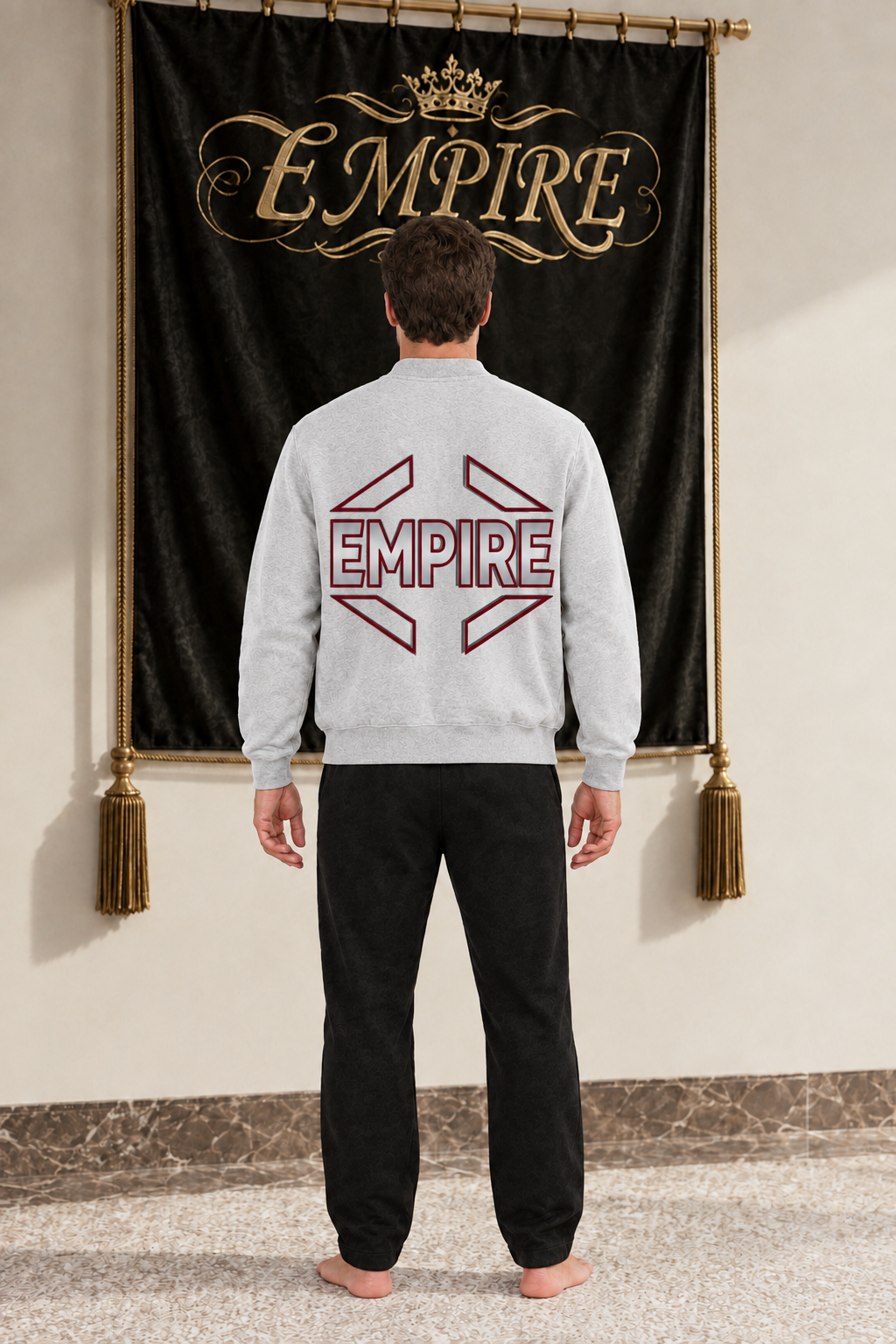 Light grey men's EMPIRE fleece zip-up varsity jacket with lower-positioned burgundy-and-charcoal geometric back wordmark, rear view on barefoot male model