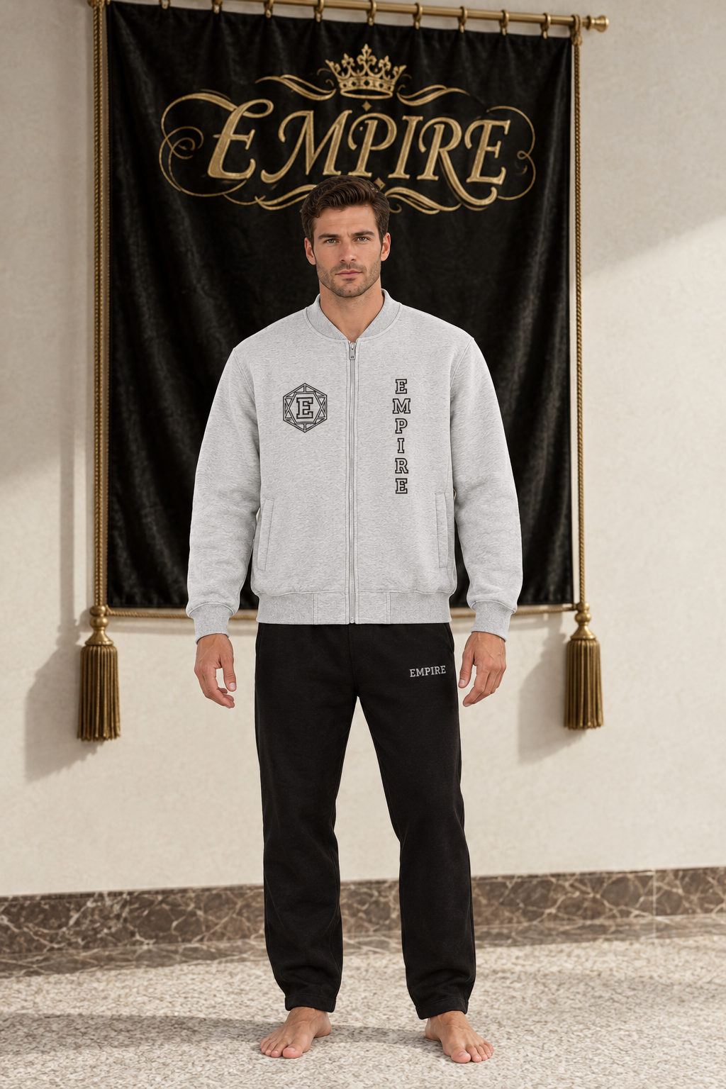 Light grey men's EMPIRE fleece zip-up varsity jacket with geometric E crest and vertical chest wordmark, front view on barefoot male model